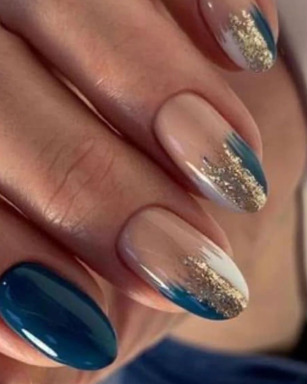 A set of oval nails in deep peacock teal and nude with gold leaf laid at the free edge.